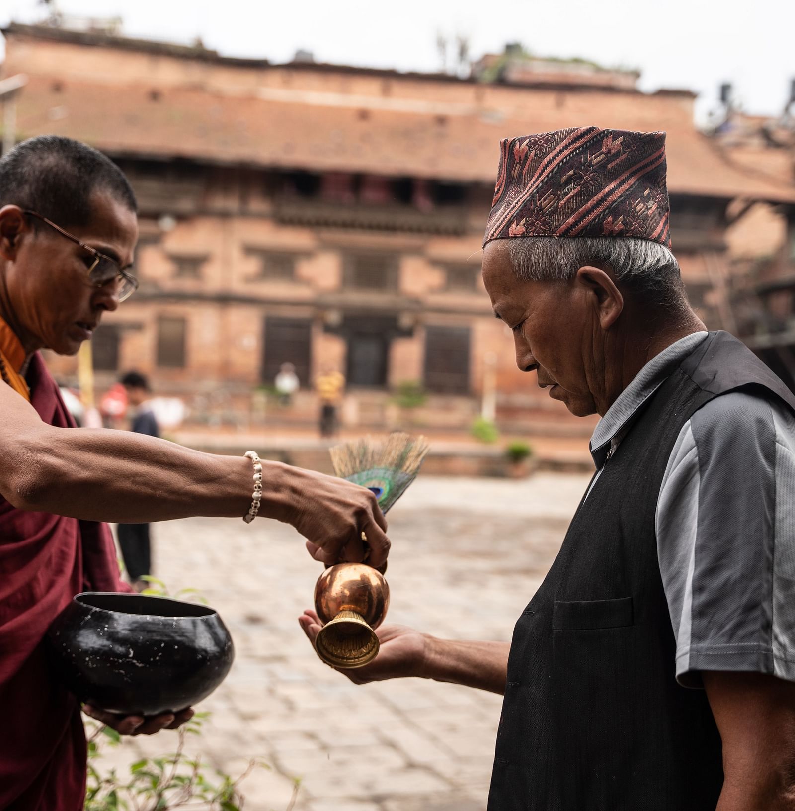 A monk pouring holy water into the palm of an old man