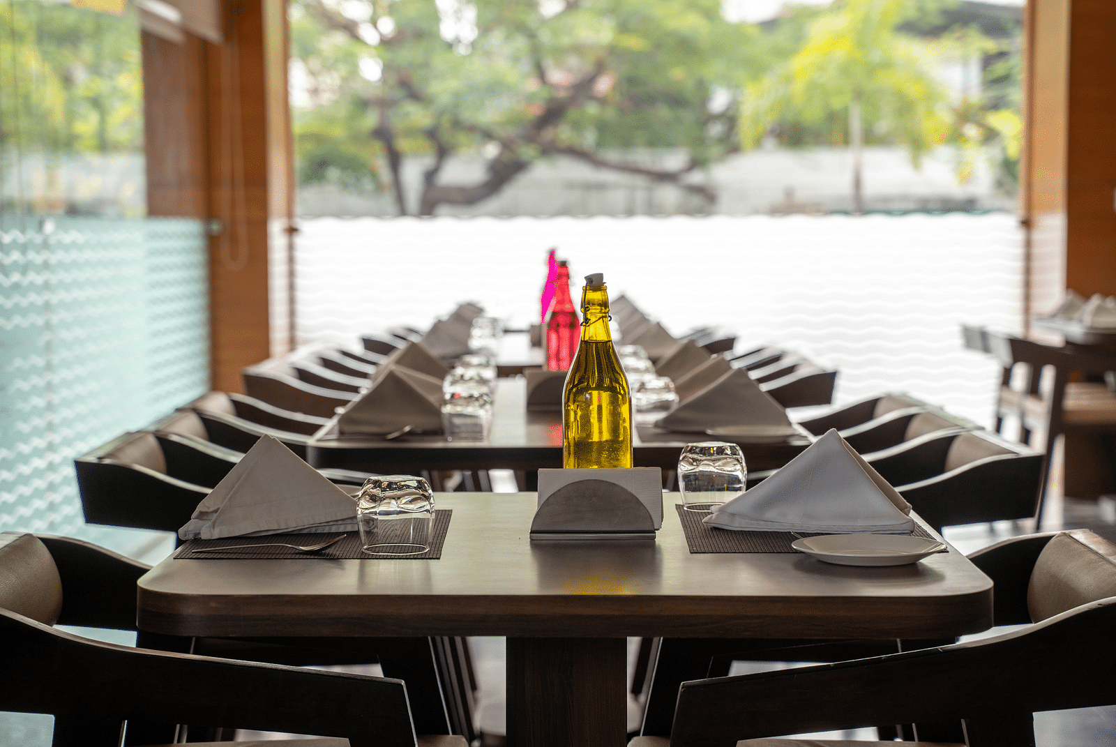 An outdoor dining area with wooden tables, neatly folded napkins, and decorative bottles - Hotel Udai Median, Udaipur.