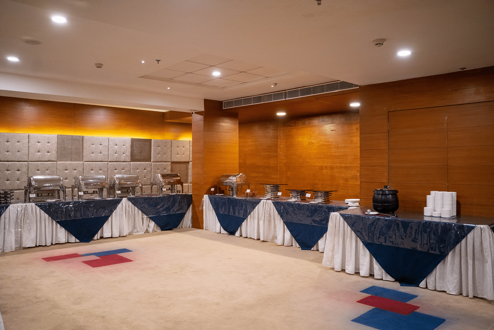 A spacious banquet hall with a stage setup and tables draped in white and blue tablecloths - Hotel Udai Median, Udaipur.