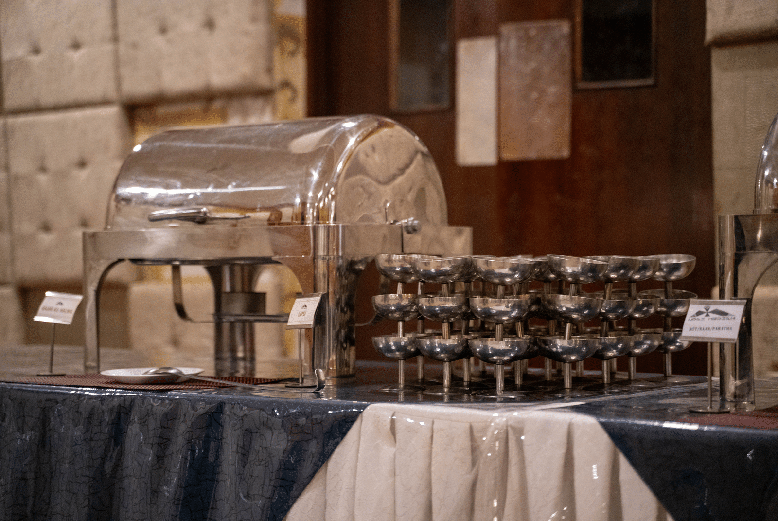 A buffet station with a stainless-steel chafing dish and neatly arranged serving glasses - Hotel Udai Median, Udaipur.