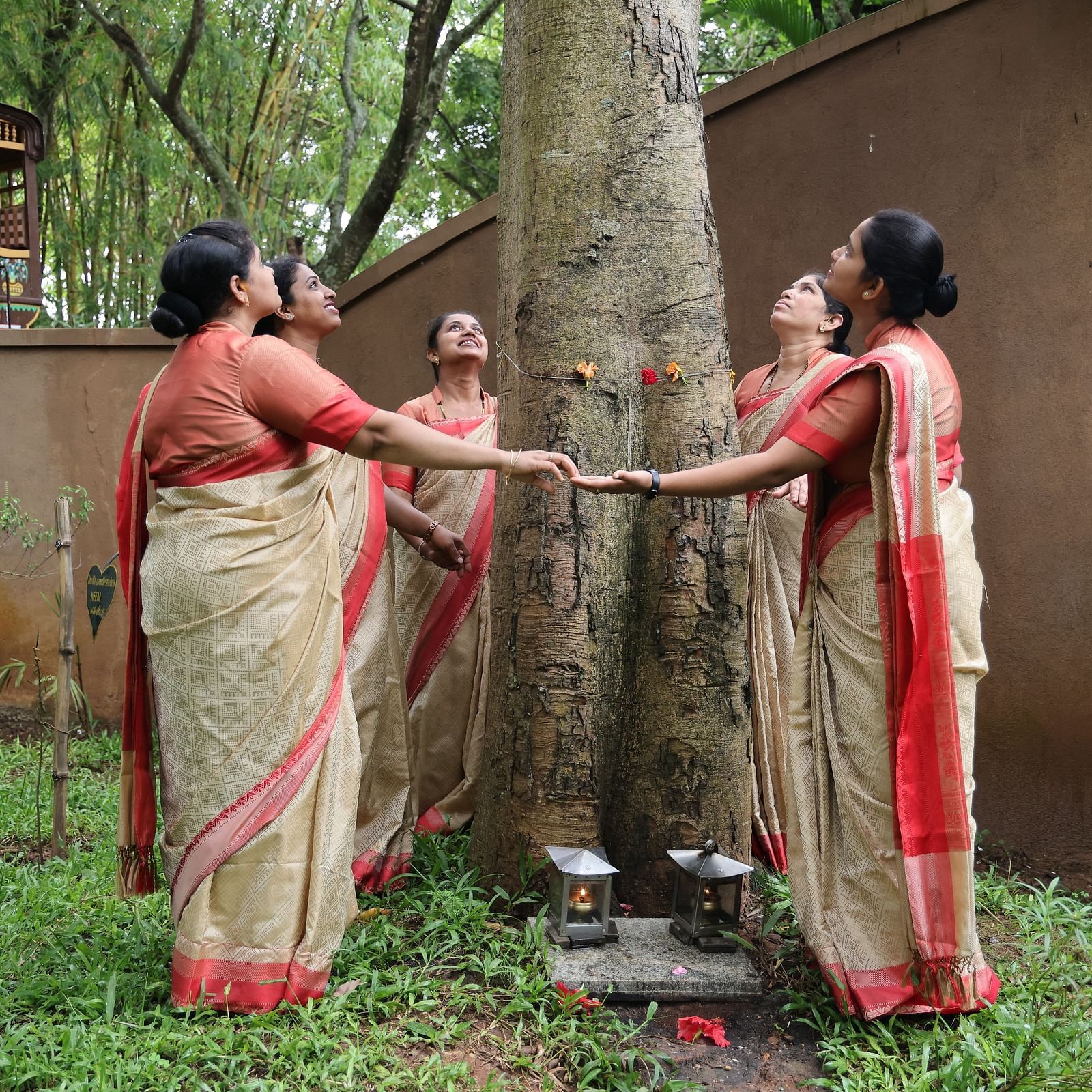 image of a group of women dressed in saree holding hands as they surround a tree at hoysala village resort in hassan