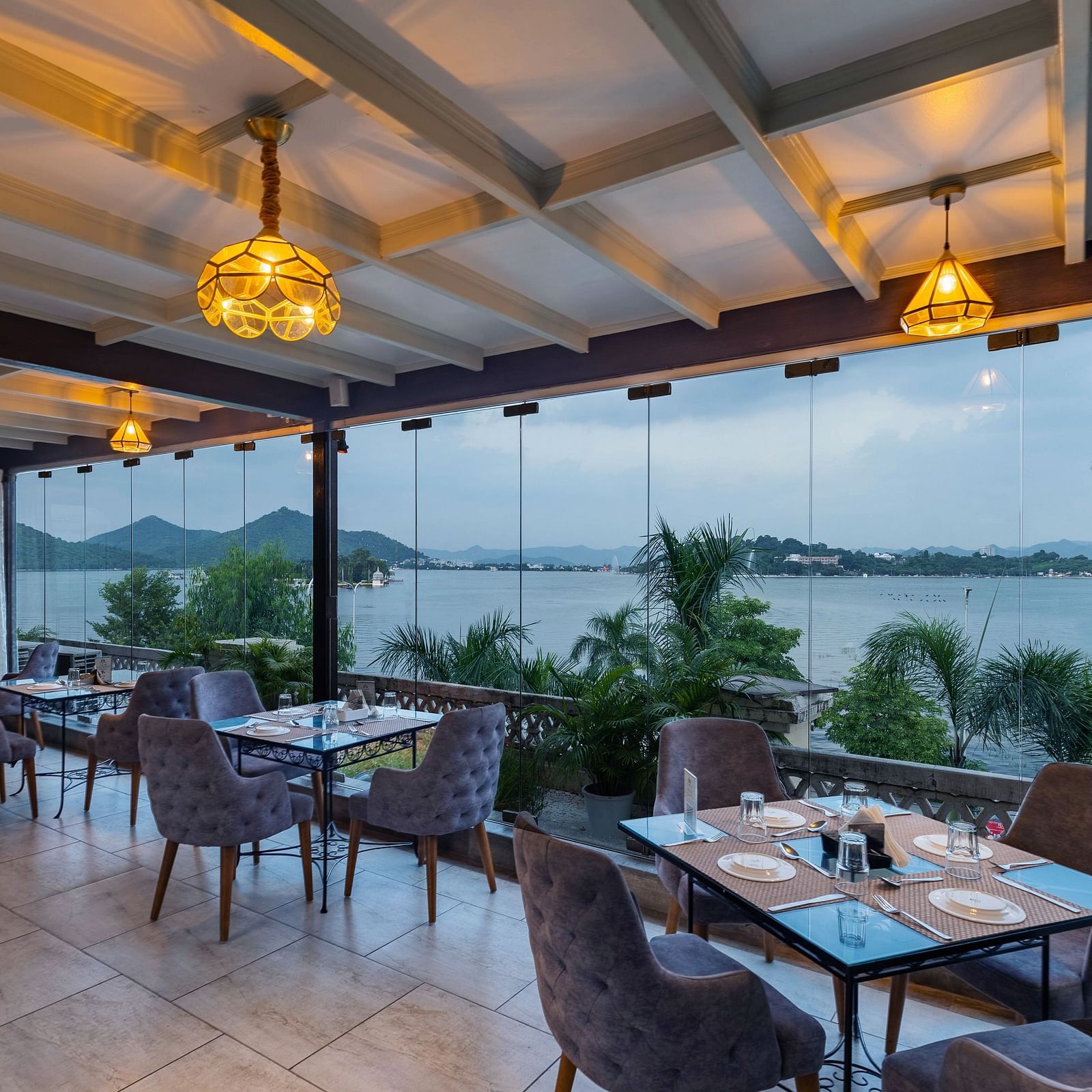 Restaurant area at Panna Vilas Palace includes a four-seater table surrounded by wooden chairs, complemented by warm lighting and potted plants | Panna Vilas Udaipur