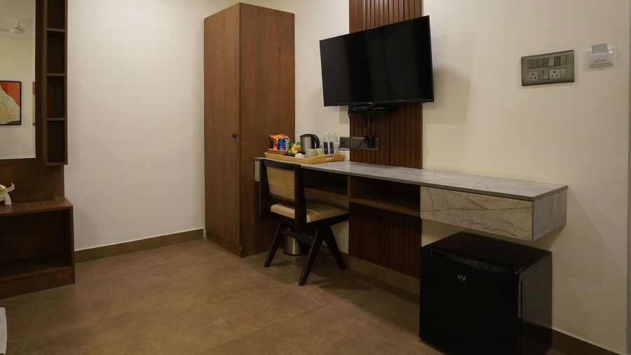 A room with a minimalist design, featuring a wall-mounted TV, a desk with a mirror, and ample lighting at Hotel Kyzen Smartstays – Smart, Reliable, Kyzen