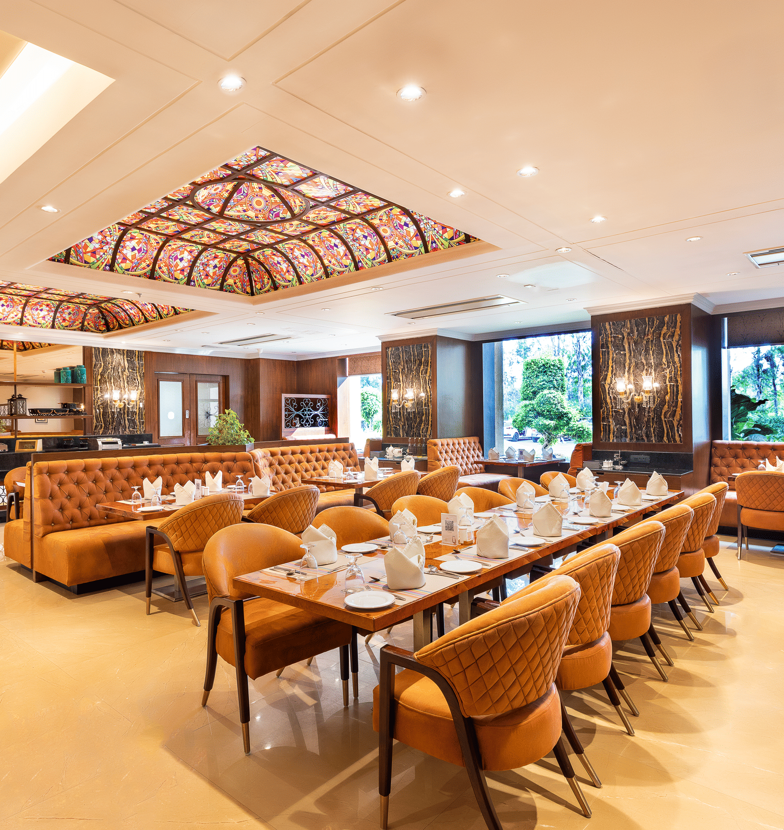 Long view of the spacious restaurant with multiple dining tables, comfortable seating, and a view of the outside through windows at Hotel Hukam's Lalit Mahal.