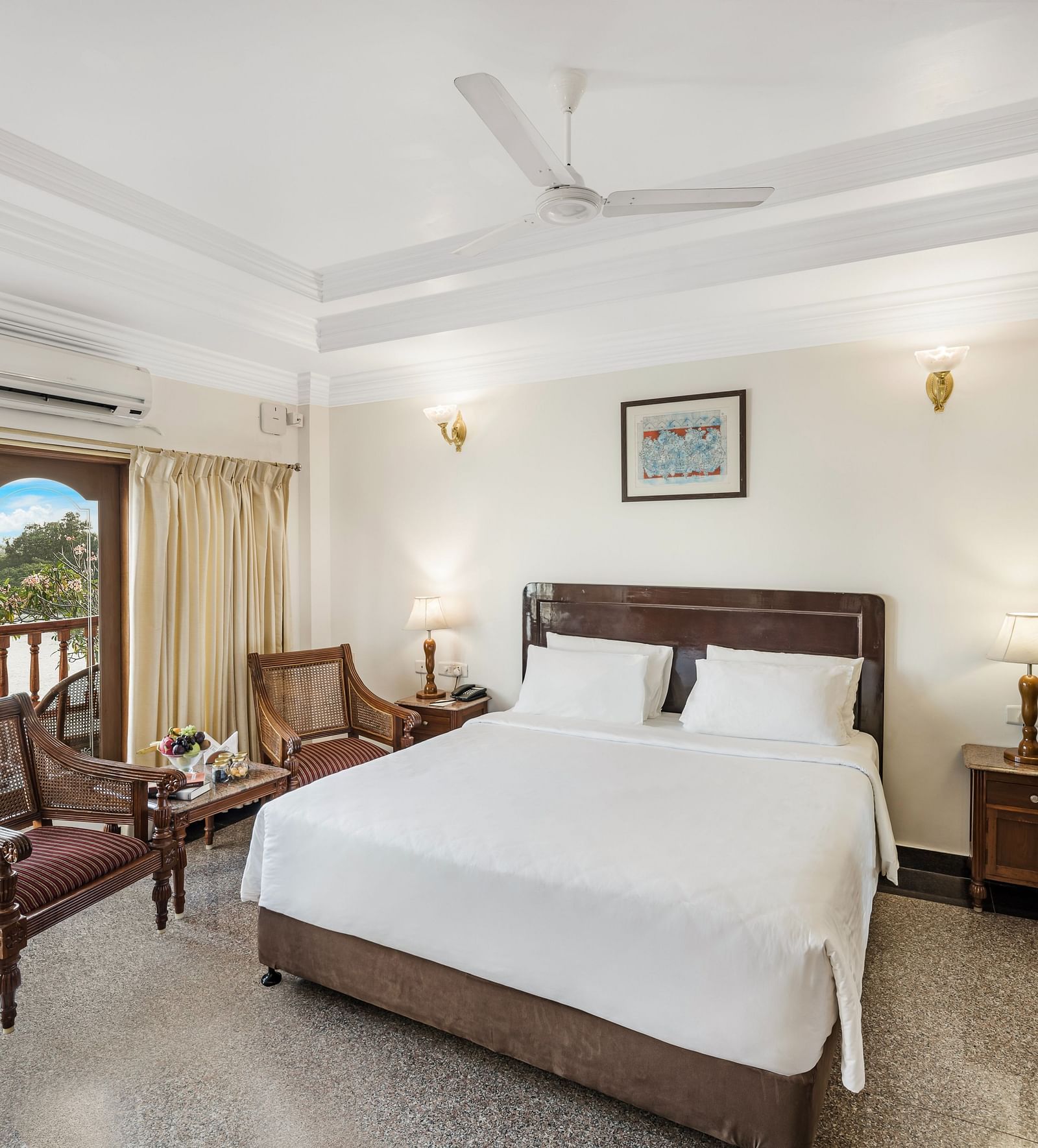 An image of the River Edge Heritage Room featuring a queen size bed, bed side table, lamps, and chairs - GReaT Trails River View Resort Thanjavur By GRT Hotels