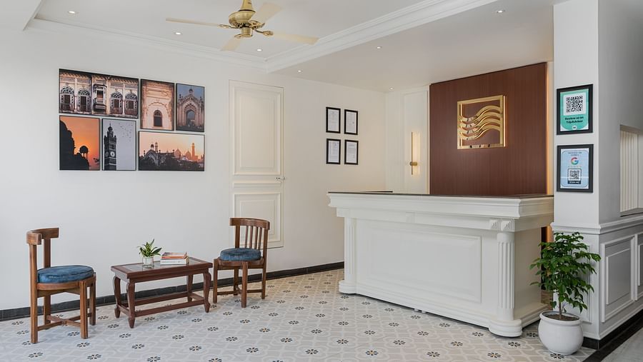 Reception area features a large desk with wall-mounted photo frames, and a pair of wooden chairs and a table in the middle | Hotel Ganga Maiya