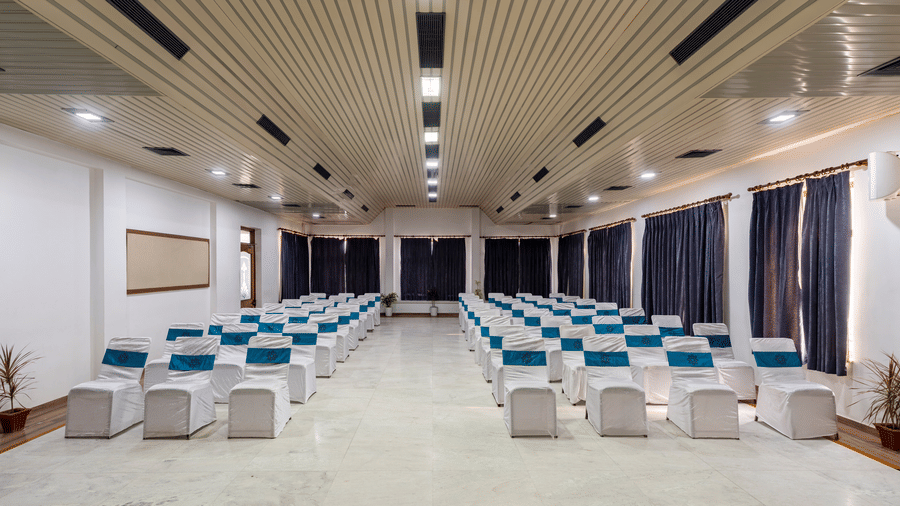 An indoor auditorium layout with rows of chairs with blue sashes facing an open floor space at Amantra Shilpi Resort, Udaipur.