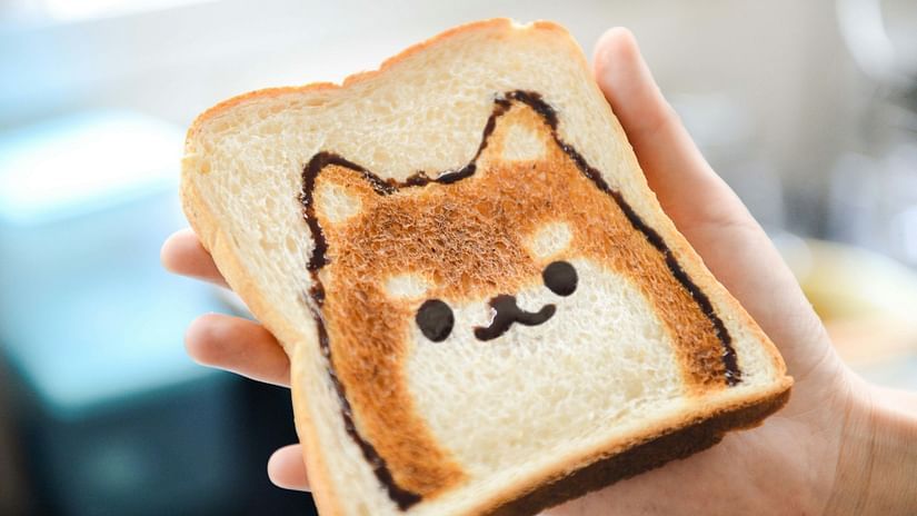 A hand holding a slice of toasted bread with an adorable cat face design made using chocolate or jam, creating a cute breakfast presentation. 