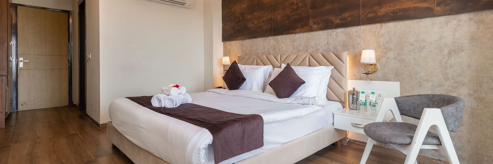 An image of the deluxe room featuring a bed with pillows and cushions, bed side tables, a chair and warm lighting - DLS Ganga Bliss, Haridwar