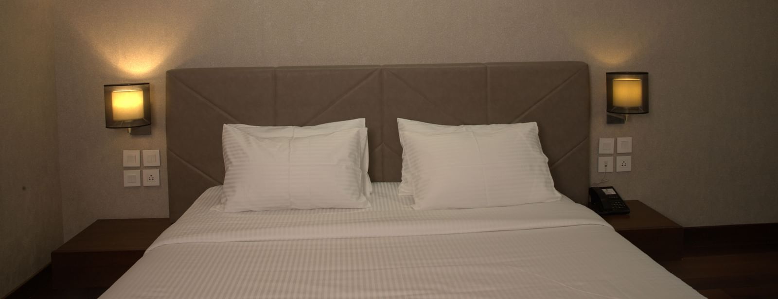 A bedroom with a large bed, bedside lamps, and elegant wall-mounted light fixtures at The Hamuse Hotel, Kodaikanal.