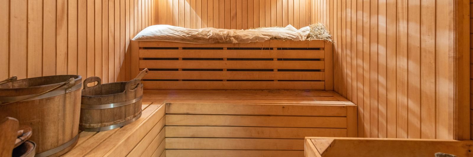 A steam room with wooden interiors and steel utensils, warmly lit.