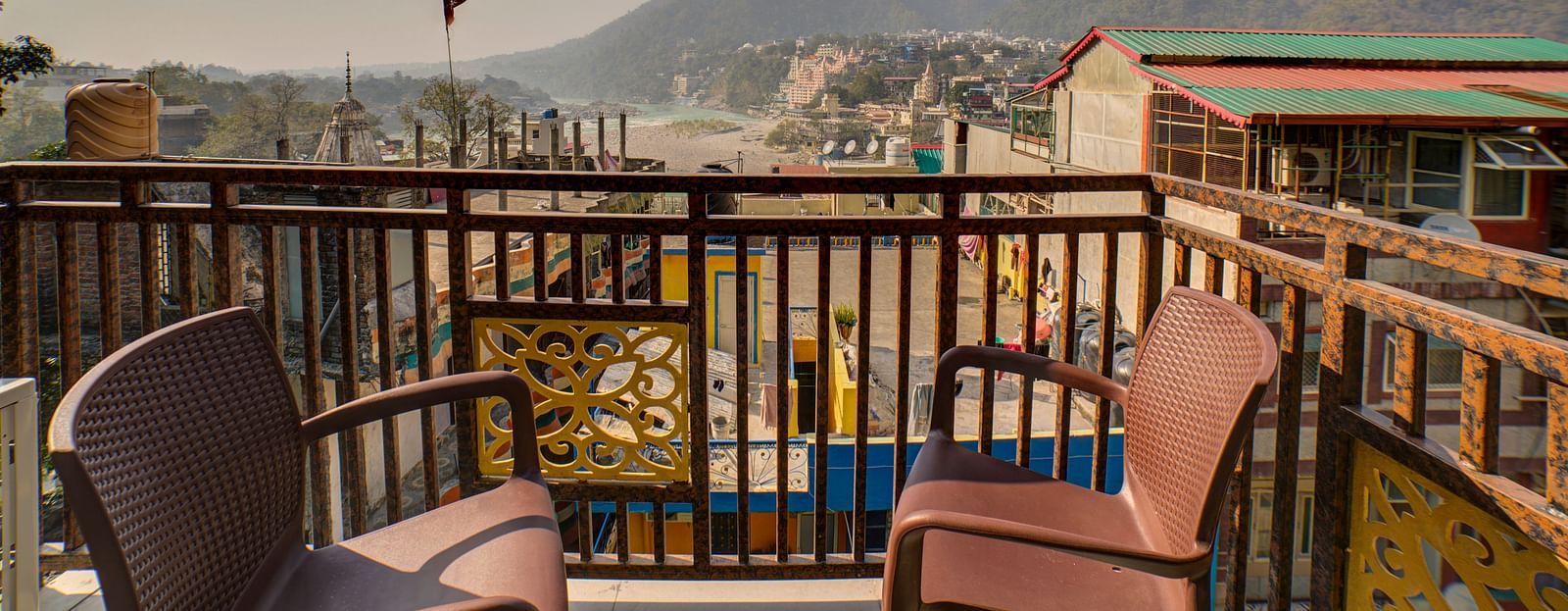 Two chairs kept on a balcony with views of mountains in the distance and the ganges river - Bedzzz, Rishikesh