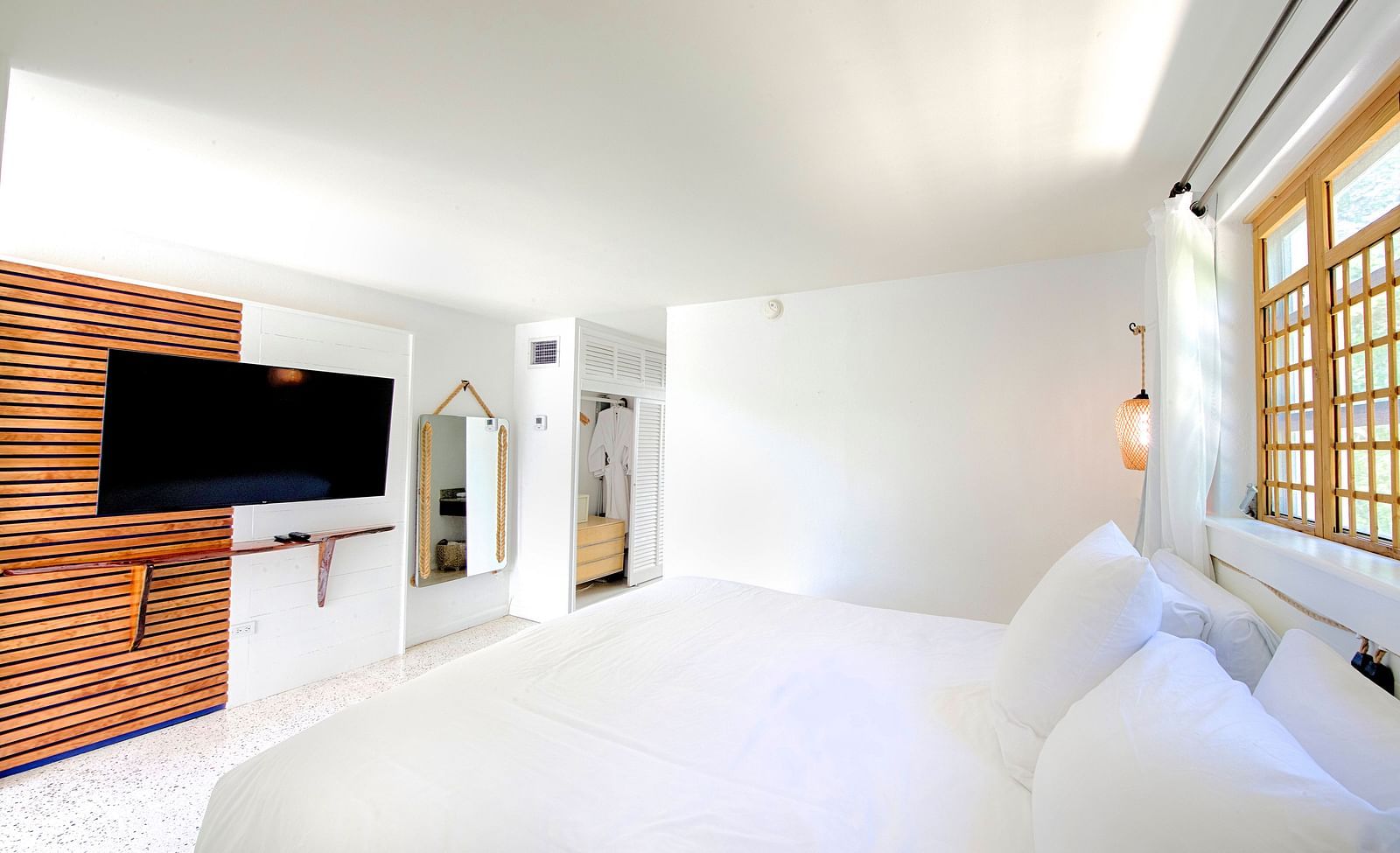 Bright bedroom at Casa Morada featuring a white bed, wall-mounted TV, and sliding wooden doors.