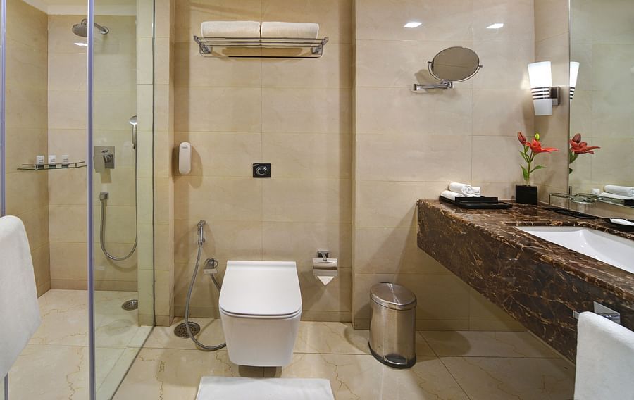Modern bathroom with glass-enclosed shower, wall-mounted toilet, and elegant vanity at The Bristol Hotel, Gurgaon.