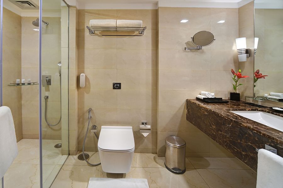 Modern bathroom with glass-enclosed shower, wall-mounted toilet, and elegant vanity at The Bristol Hotel, Gurgaon.