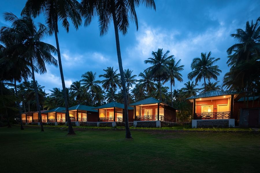 a far out view of cottages with coconut trees and dark sky in the background