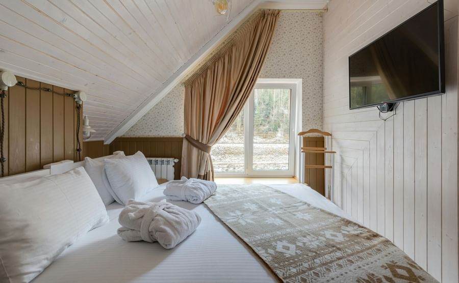 An attic-style room featuring twin beds with white linens on them and a wall-mounted TV.