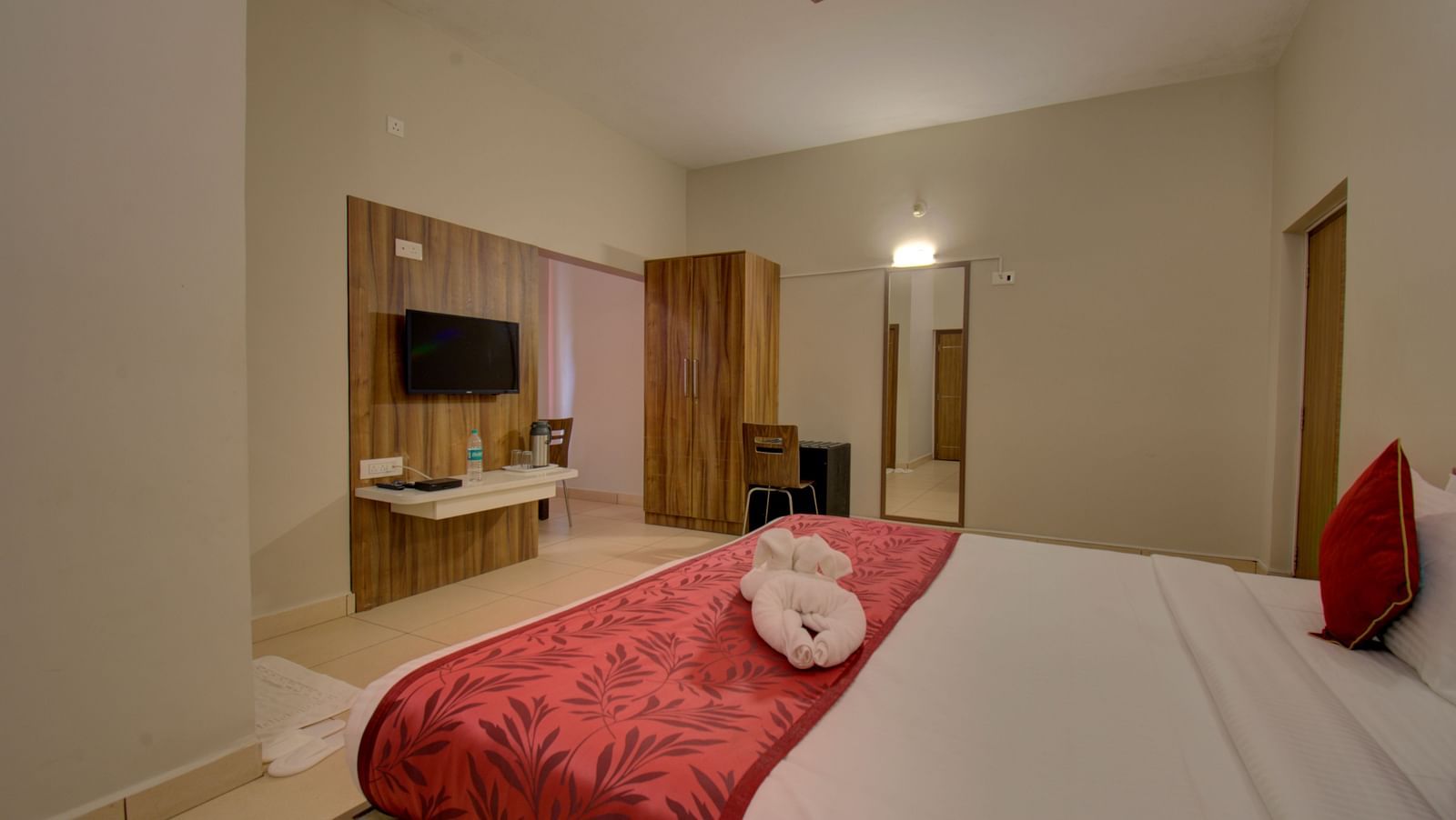 A bedroom with a bed, TV, mirror, and wooden doors | Superior Room | Woodstock Resorts, Coorg