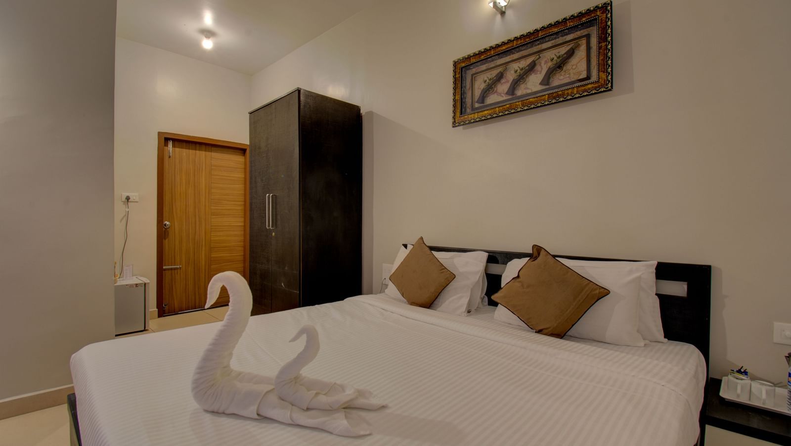 Swans made with towels on a huge bed, a cupboard, side table, a wall art and wooden door | Superior Room | Woodstock Resorts, Coorg