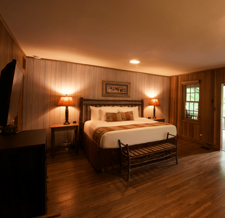 a dimly lit room featuring a double bed along with a bunk bed in the corner with a door opening to the exterior of the cabin - Historic Tapoco Lodge