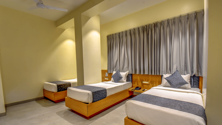 Delxue Triple Room at VITS Select Nashik Hotels & Resorts featuring 3 single beds next to each other under warm lighting against a curtained window