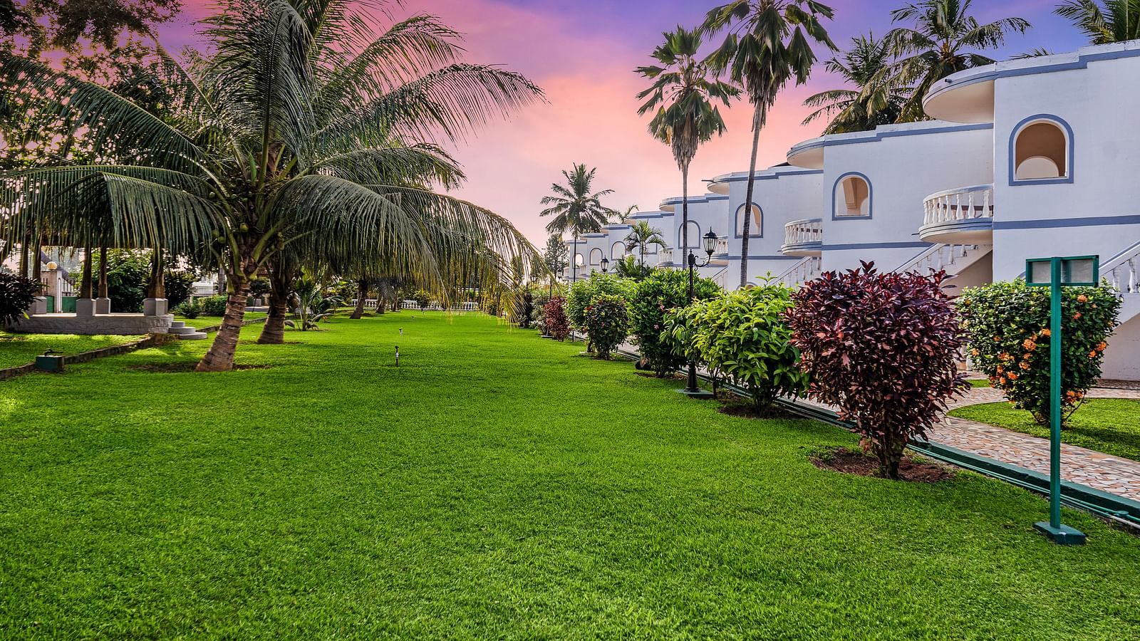 An image of the lawn with greenery and plants and the hotel building in the background - GReaT Trails River View Resort Thanjavur By GRT Hotels