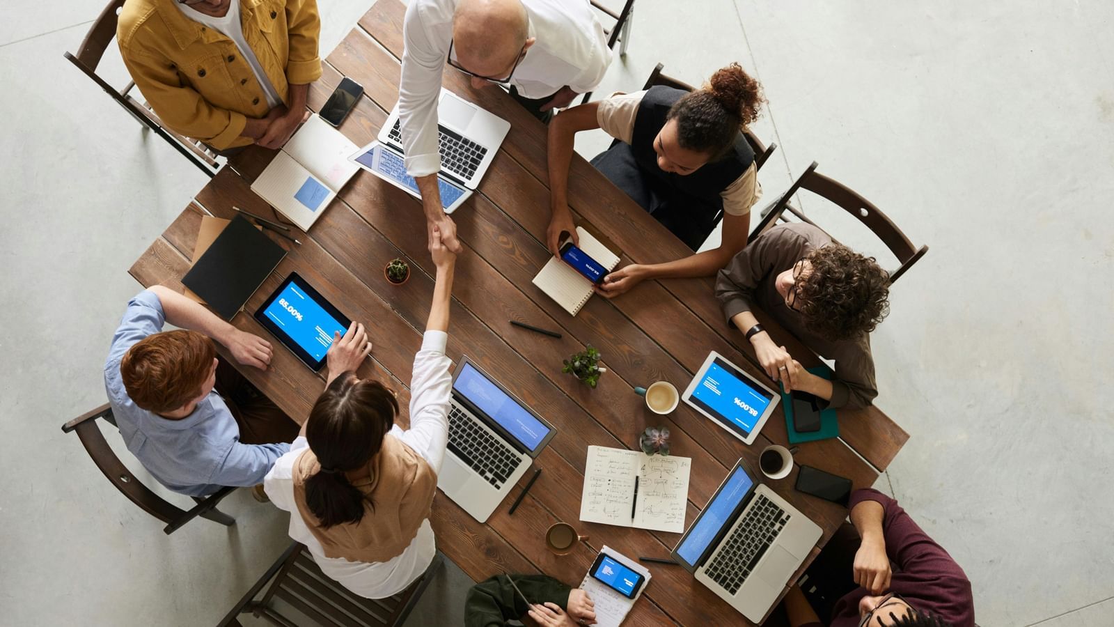 Overhead view of a diverse group of people collaborating around a table with laptops and tablets in an office setting.