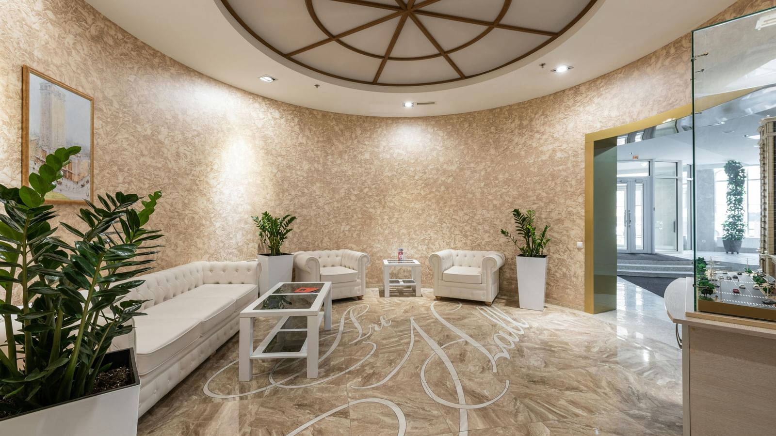 A luxurious hotel reception are with a plant, glass door and marble floors with seating