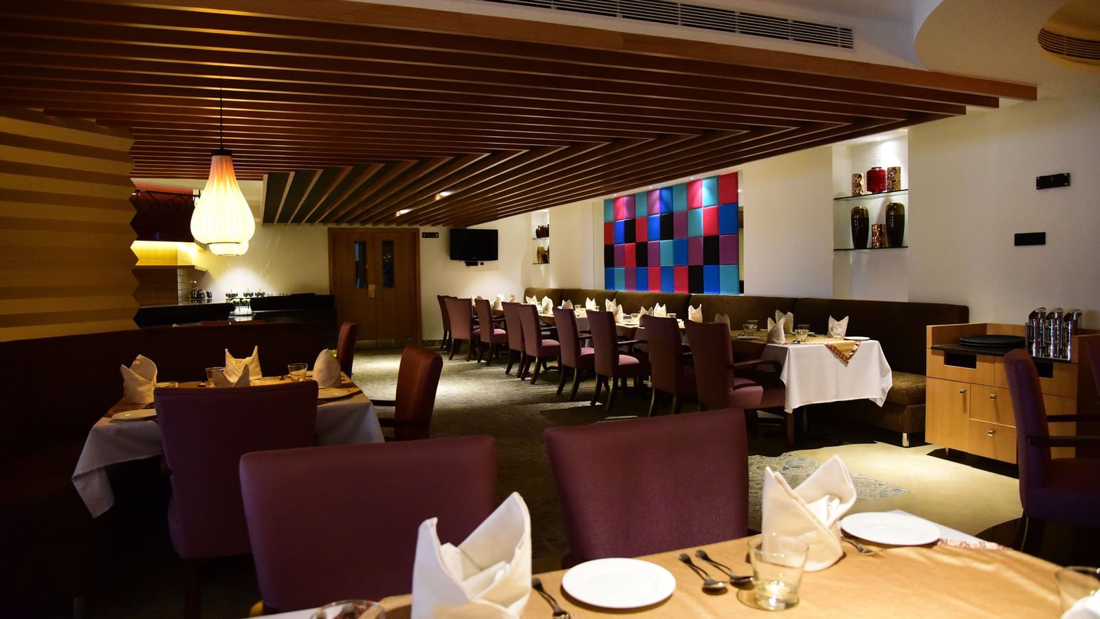 A side-angle shot of a hotel restaurant at The Royal Comfort, with elegant lighting, tables set for dinner, and a warm atmosphere.
