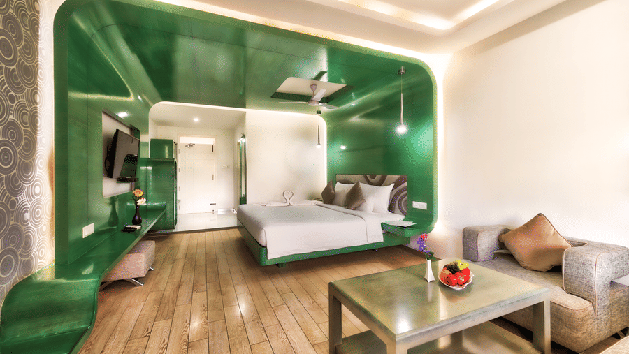 A room with king size bed, green wall panel, and a seating area at Grande Bay Resort & Spa, Mamallapuram.