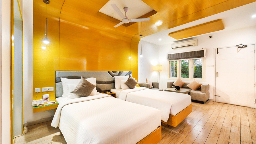 A room with twin beds with golden panel wall and wooden flooring featuring a seating area at Grande Bay Resort & Spa, Mamallapuram.