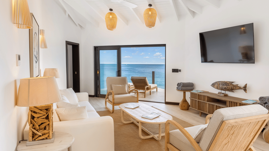 A living room with chairs, a sofa, a table, a television, and glass doors opening to a view of the ocean at Tamarind Hills Resort and Villas, Antigua.
