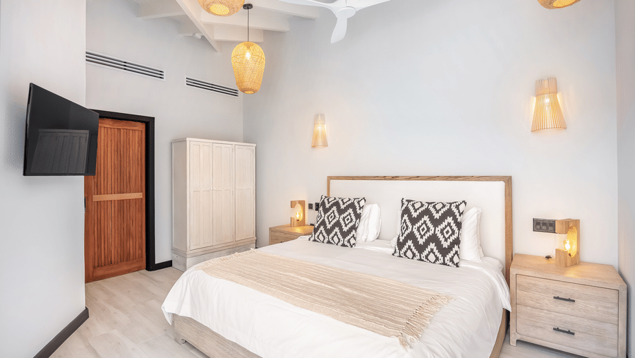 A bedroom at Tamarind Hills Resort and Villas, Antigua, with a king size bed with bedding, a lamp upon a nightstand, a wall mounted television and a door.