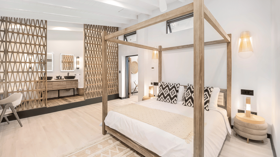 A bedroom featuring four-poster bed, wood pattern wall, and a pathway to a living room at Tamarind Hills Resort and Villas, Antigua.