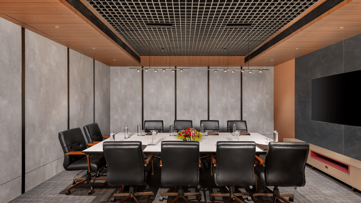 Boardroom at Voyage Milestone Hotel and Banquet featuring chairs around a table with 2 chairs facing the monitor mounted on the wall and flower vase and water bottles on the table
