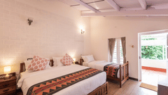 The warmly lit Oxford room at Ibex Resorts, Coonoor (Leewood), with a large bed, bespreads, pillows, and door leading to the outer end.