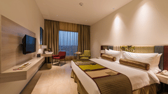 Contemporary guest room with twin beds, wall-mounted television, work desk and large window at Pride Elite Phaltan.