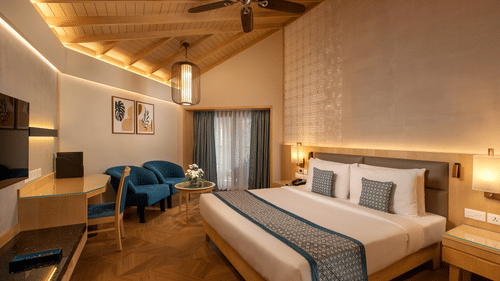 A view of the Superior Deluxe Room with a king bed, side tables, lamps, a tv, ceiling fan, chairs in the corner with a coffee table at Kenilworth Resort & Spa, Goa, one of the best workation places in Goa.