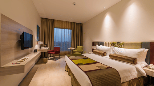 Contemporary guest room with twin beds, wall-mounted television, work desk and large window at Pride Elite Phaltan.