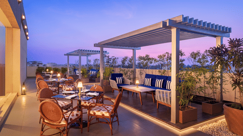 A rooftop restaurant at Sarovar Portico, Hanumangarh, with tables, chairs, and benches.