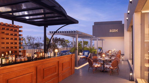 A bar with a wooden counter and a rooftop restaurant at Sarovar Portico, Hanumangarh, with tables and chairs.