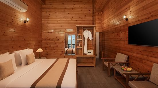 A hotel room in sindhudurg featuring a double bed, a wall-mounted television, a wardrobe with bathrobes and furniture to unwind - Highland Sarovar Portico, Sindhudurg