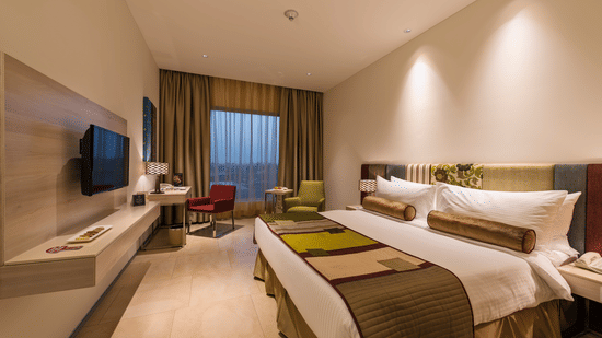 Contemporary guest room with twin beds, wall-mounted television, work desk and large window at Pride Elite Phaltan.