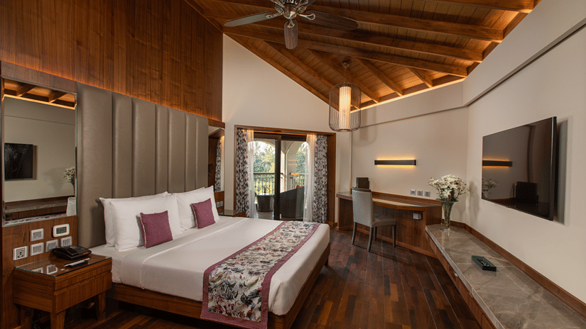 Pool View Suite King Bed looks neat in a mostly-white bedding surrounded by white walls and wooden furnishing at Kenilworth Resort & Spa, Goa