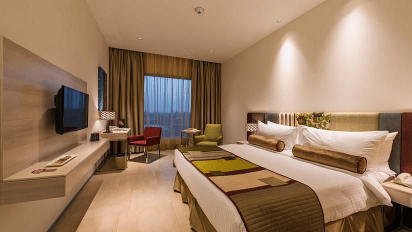 Contemporary guest room with twin beds, wall-mounted television, work desk and large window at Pride Elite Phaltan.