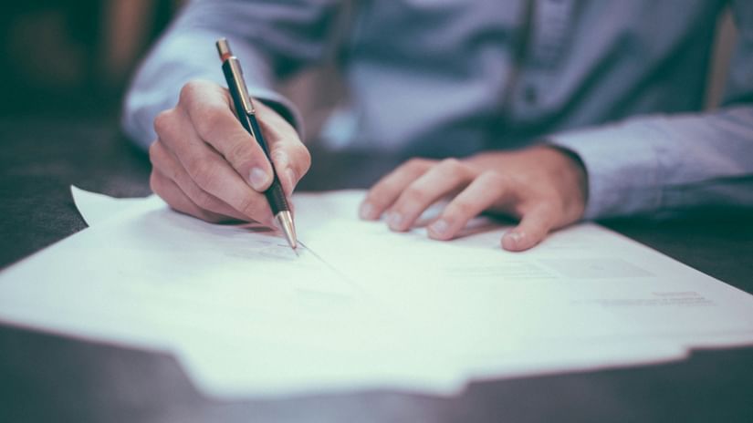 A close up of a person signing some documents placed on a table.