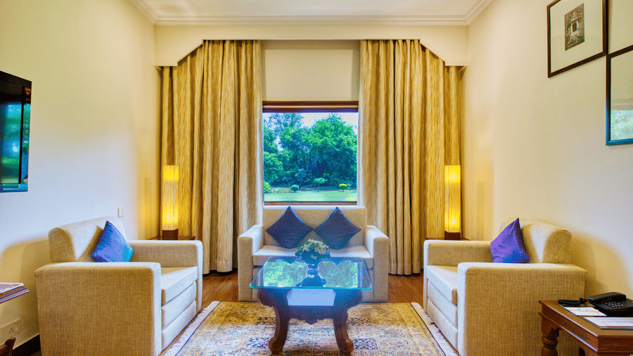 An Premium Suite living area at Clarks Khajuraho with armchairs, a center table, a television, and large curtains opening to a window view.