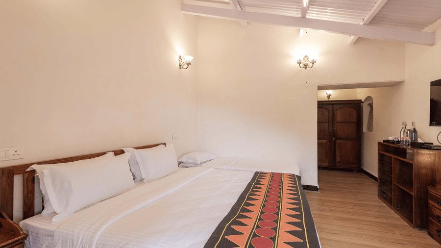 The well-lit cambridge at Ibex Resorts, Coonoor (Leewood), featuring a large bed, bedspreads, pillows, and a television.