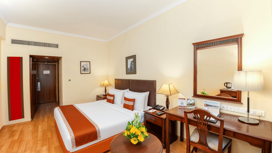 A room with a large bed, spreads, pillows, chairs, and a door. | MGM Mark Whitefield