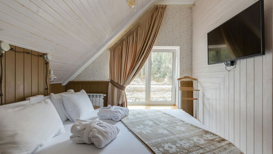 An attic-style room featuring twin beds with white linens on them and a wall-mounted TV.